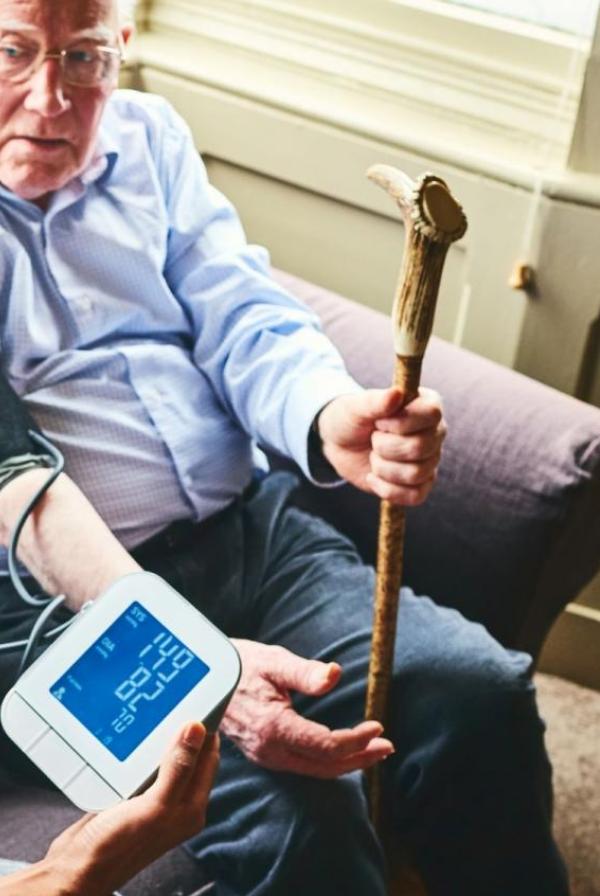 GP taking blood pressure of older man at home visit